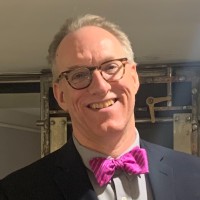 Professional headshot of Bruce Richard, Director at MCLE New England, wearing glasses and a pink bow tie.