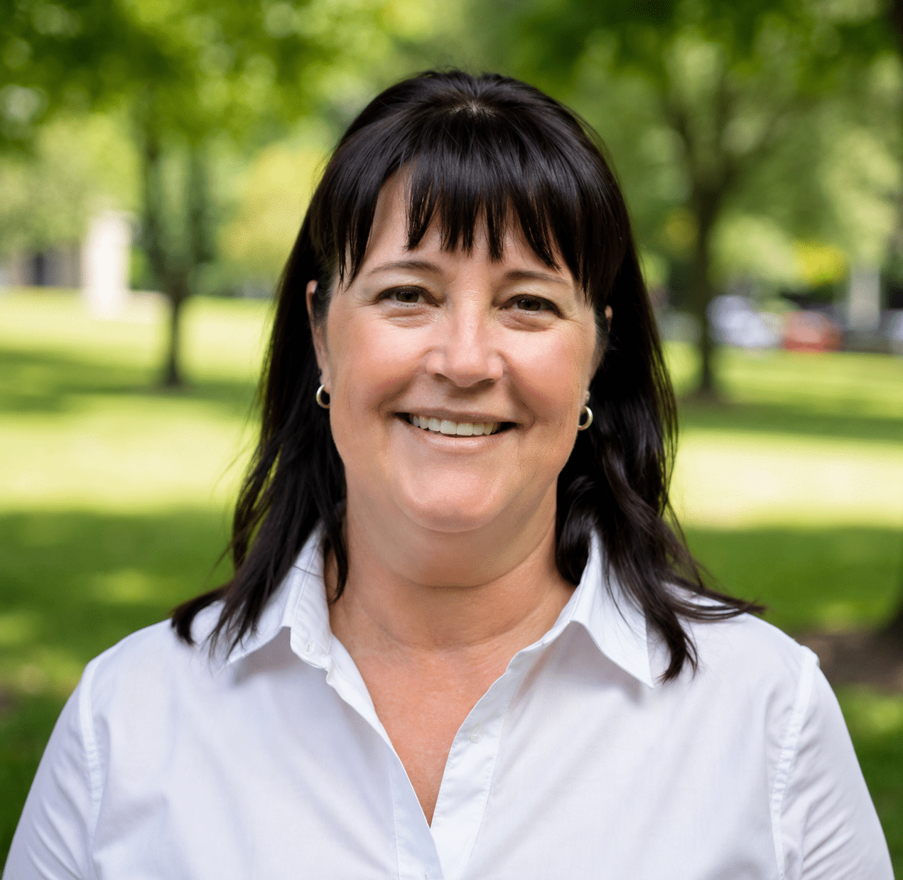 Professional headshot of Kelley Brubaker, CPA and founder of Profit, Scale, Thrive, smiling in a white collared shirt in front of an outdoor park setting.